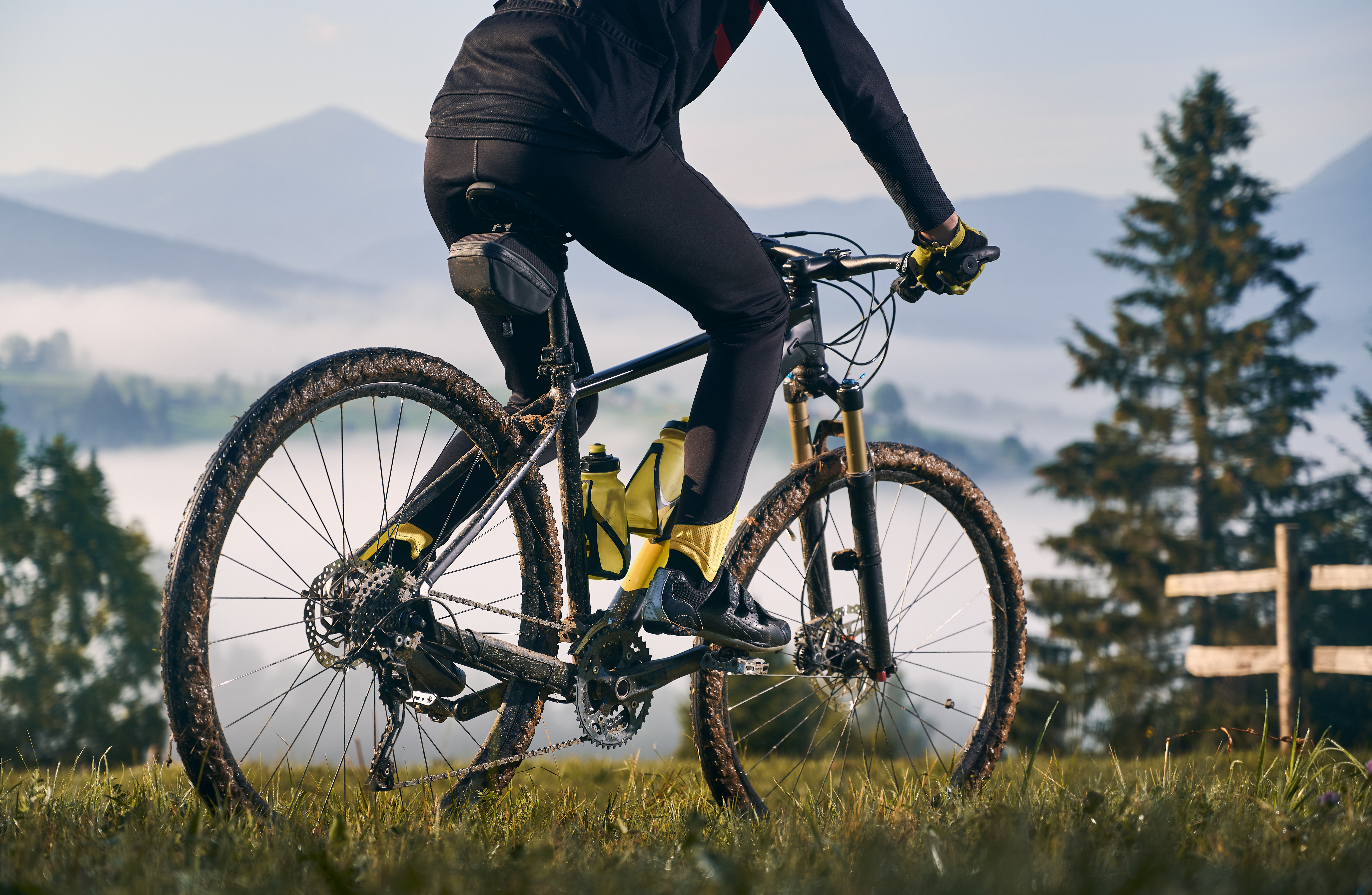 Close up view of man cyclist in cycling suit riding bicycle on grassy hill. View of majestic mountains on the blurred background. Concept of sport, bicycling and nature.